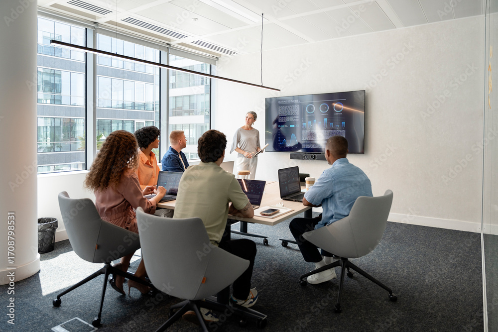 © Santi Nuñez/Stocksy - Business team analyzing charts on a large screen during meeting