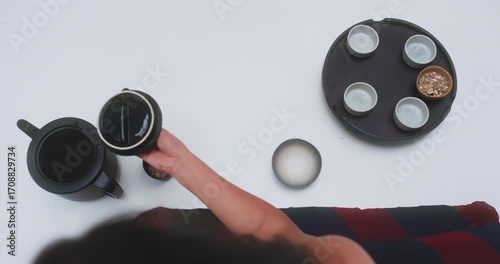 Overhead view of woman lifting teapot lid beside tea tray