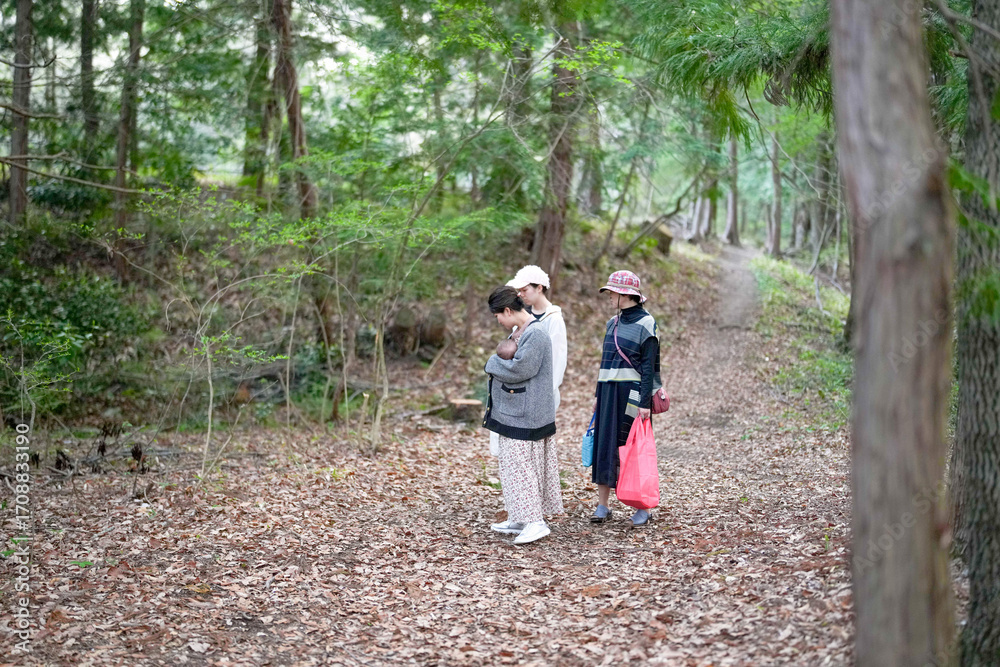 Fototapeta premium Three people are walking in a forest, one of them holding a baby. Scene is peaceful and serene, as the group is surrounded by nature and enjoying a quiet walk