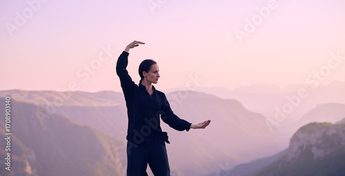Quadro su tela Woman practicing Tai Chi in traditional black outfit on mountain at sunrise, arms outstretched in meditation pose focusing on balance, energy, and mindfulness in nature