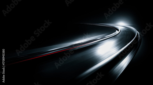 Dark road with a bright light shining on it. The road is curved and the light is coming from the side