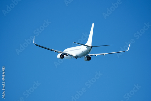 Tableau sur toile The plane that's just taken off drifts away from the airport across clear blue sky