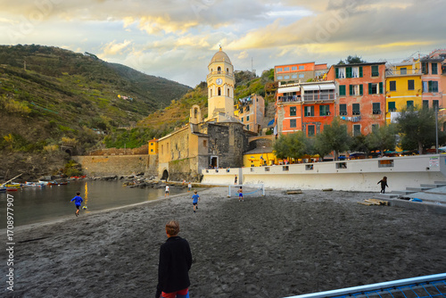 Fototapeta Naklejka Na Ścianę i Meble -  A group of local young Italians play soccer football on the small beach and marina at dusk in the colorful Cinque Terre village of Vernazza, Italy.