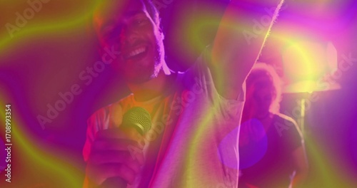 Singing singer holding mic and raising arm on club stage with colorful spotlights and lens flare