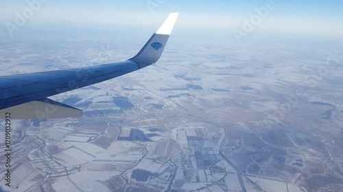 Snowy land and plane wing seen from passenger window view.