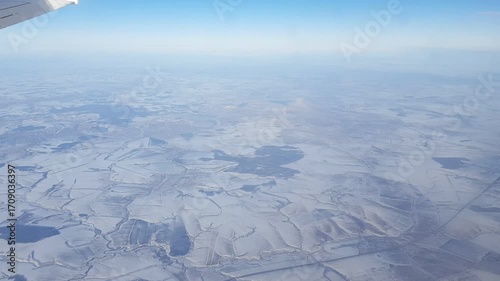 Land view from plane window seat, snowy fields below.