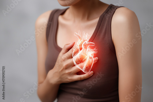 A woman in a brown tank top clutching her chest with a glowing anatomical heart illustration, symbolizing heart pain or cardiovascular issues