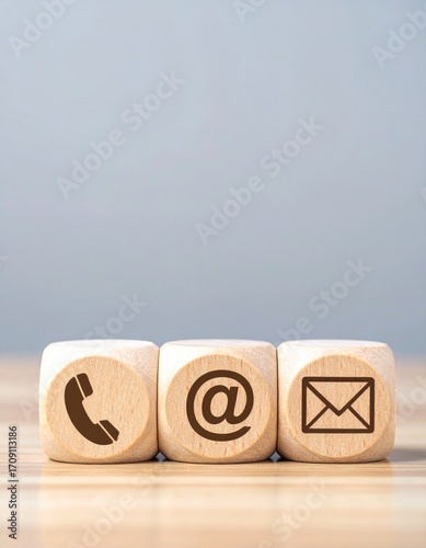 Three light wooden cubes showcase contact icons phone, at-sign, and email, set on a wooden surface against a soft gray backdrop