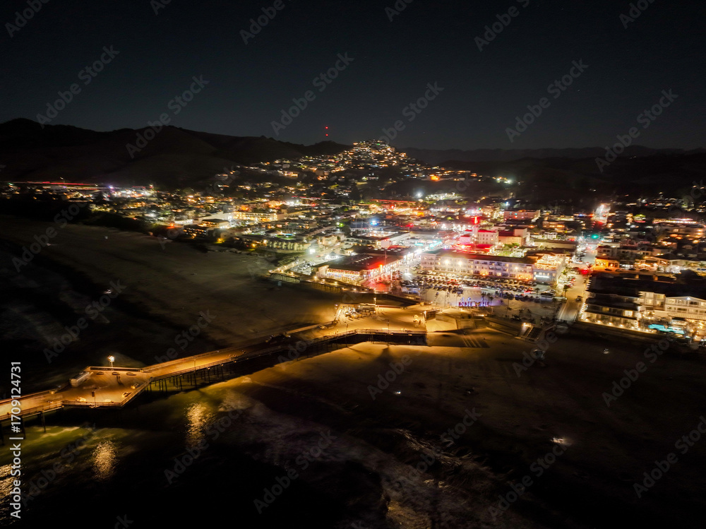 Obraz premium Pismo Beach, California, USA, September, 16, 2025: Pismo Beach, California, As seen from a UAV Drone at night looking at City Downtown and the Pier Beach Area with the colorful lights of the night.