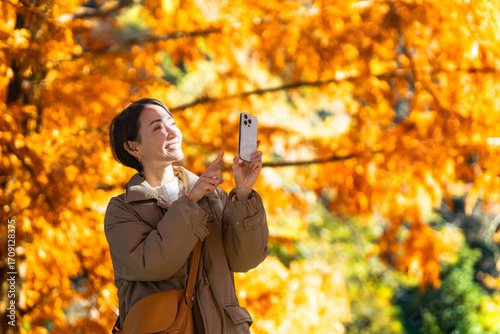 紅葉をスマートフォンで撮影している女性　ライフスタイルイメージ