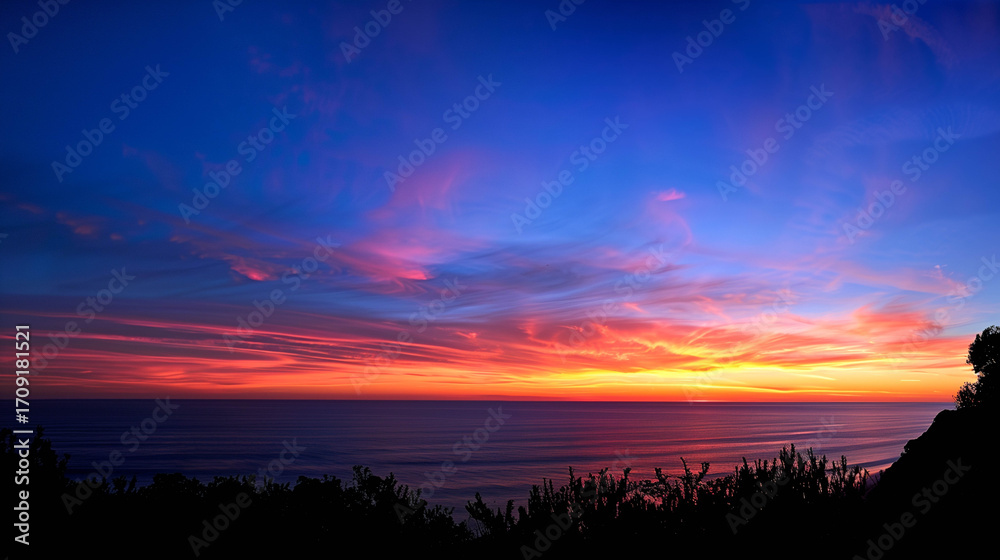 Fototapeta premium Stunning sunset over the ocean with vibrant colors and silhouetted foreground vegetation