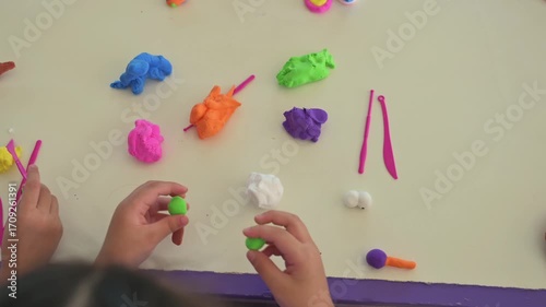 Children on a table combining play dough and colorful clay. Clay play activity for early education, creative children's hand activities, enjoyable learning, and combining vibrant colors.