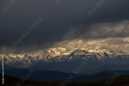 Sunlit Peaks Beneath Stormy Skies – Dramatic Snow-Covered Mountain Landscape