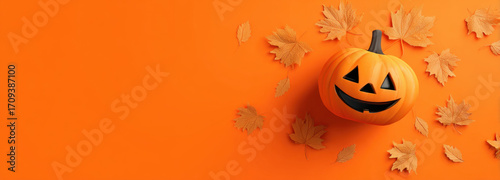 Cheerful Halloween pumpkin with carved face sits on vibrant orange background, surrounded by autumn leaves, creating festive and playful atmosphere