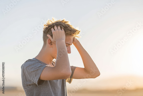 teenager in moment of contemplation compresses their head with their hands against clean solid background