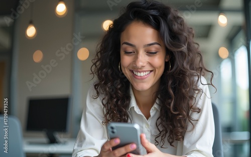 Smiling portrait with latin hispanic woman working on smartphone in office for e shopping or studying. Young indian specialist using cell phone mobile app for work business chat, looking at copy space