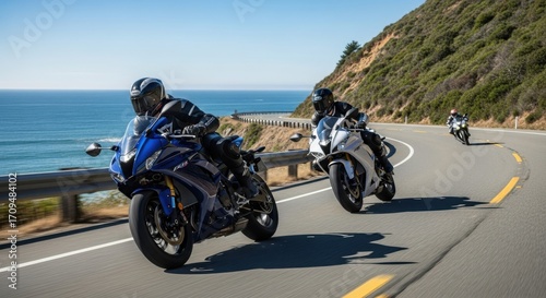 Two sport motorcycles ride along a scenic coastal highway with the ocean on one side and a lush green hill on the other