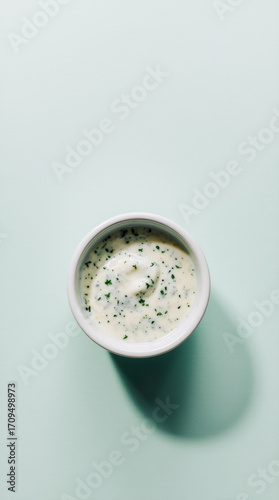 Ranch dressing with herb flecks in a white ramekin on a pastel mint background, clean top-down studio shot with soft halo shadow