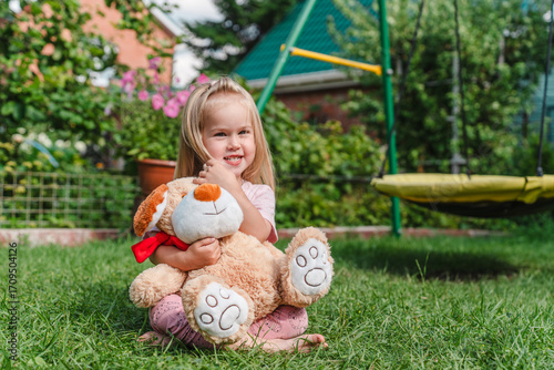 Konstfotografi Caucasian child girl hugs a big toy bear in the garden in summer