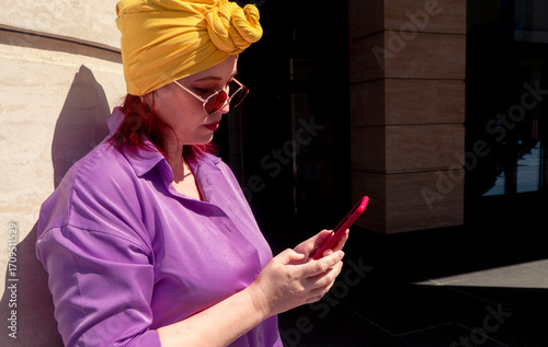 Happy and funny cool lady with fashionable clothes on dark background look to the phone seriously and thoughtfully - adult asian with extravagant style, concepts about lifestyle, fasion and elderly