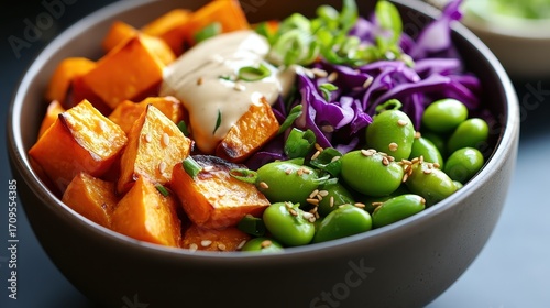 A vibrant bowl featuring roasted squash, purple cabbage, edamame, and a creamy sauce, showcasing a healthy and colorful meal.