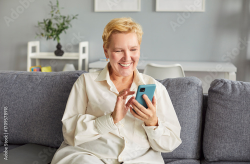 Canvastavla Cheerful mature woman radiating joy scrolls through her mobile phone, enjoying quiet moment
