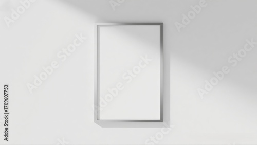 Empty framed poster with natural light casting a shadow on a white wall