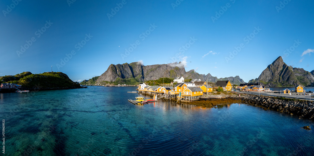 Fototapeta premium Brightly painted cabins line the tranquil waters of Sakrisoy, Lofoten, Norway, under a clear blue sky.
