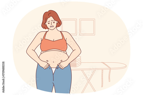 Woman experiencing problems with excess weight tries to put on small pants, and needs diet. Girl with excess weight does not fit into clothes due to appearance of belly and cellulite caused by obesity