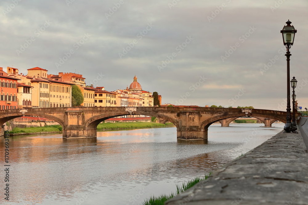 Fototapeta premium Ponte Santa Trinita Bridge east side at sunrise under a colorful cloudy sky, seen westward from Lungarno degli Acciaiuoli Road. Florence-Tuscany-329