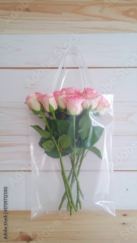 Clear plastic bag with a bouquet of pink roses on a light wooden surface