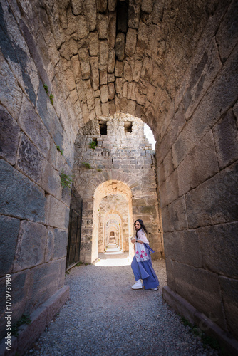 Asian woman tourist take a holiday for travel in summer at Acropolis of Pergamon Ancient Greek City, Landmark of Tourism Turkiye, Izmir, Turkey. She is standing archway area and enjoy relax vacation.