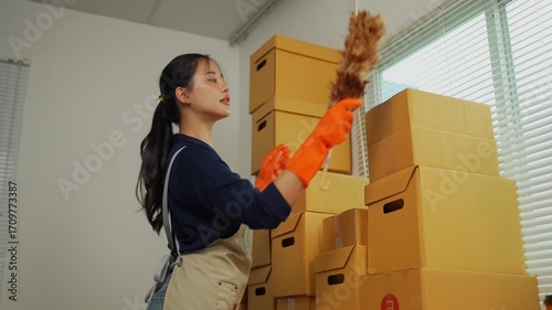 Woman cleaning stacked cardboard boxes with feather duster