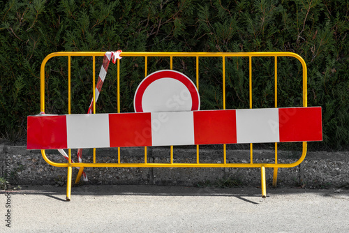 A temporary yellow road barrier features a prominent red and white striped warning board and a 