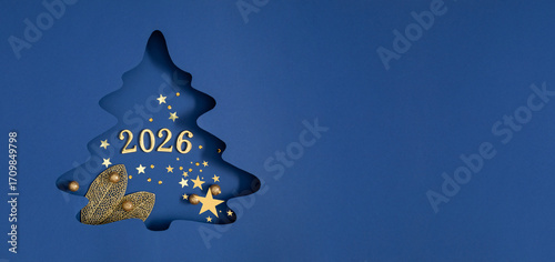 Fotografie Festive wide composition with cut-out Christmas tree and golden number 2026, decorated with Christmas tree decorations, stars and glitter on blue background, creates a New Year's holiday atmosphere