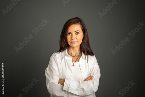 Fotografie Confident woman with arms crossed in studio setting, in white shirt on dark background in professional atmosphere