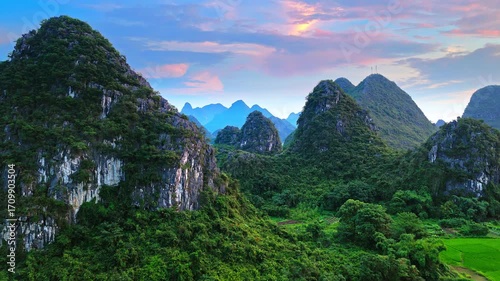 Aerial shot of the breathtaking karst mountain formations covered in lush green forest under a colorful sunset sky in Guilin, China.