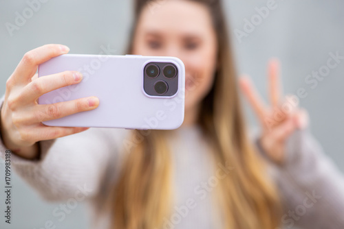 Smartphone close-up with woman making peace sign in background