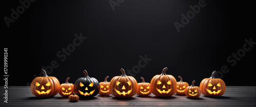A row of glowing orange and one black jack-o'-lanterns with carved spooky faces on a dark wooden table against a black background, Halloween.
