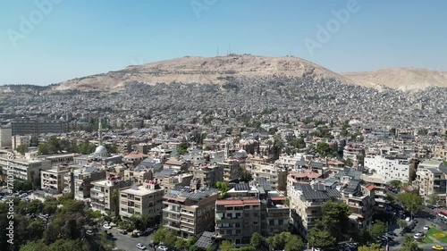 An aerial view captures the new Syrian national flag hoisted on a towering pole in central Damascus, with Mount Qasioun, one of the capital’s most prominent landmarks rising in the background.