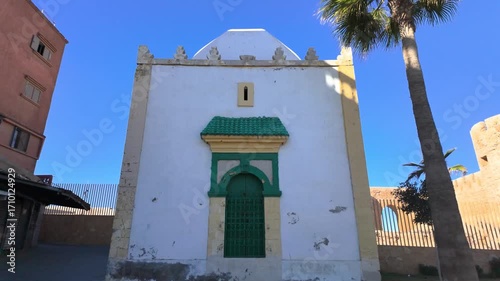 Front view of a traditional white Moroccan building with a green door in Safi, Morocco, framed by palm trees and blue sky. A striking example of local architecture and cultural charm in a coastal city