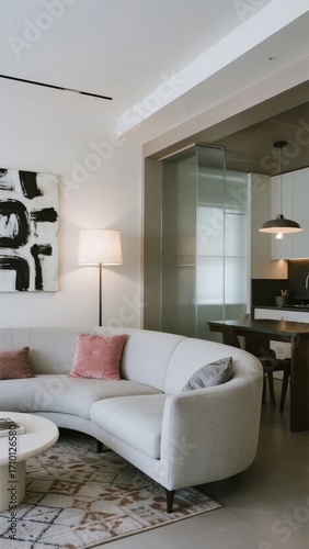 Modern living room with curved white sofa, abstract art, and open-plan kitchen area