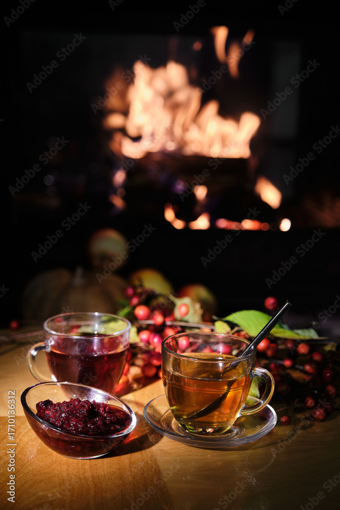 Fototapeta premium Cozy autumn scene with tea, jam, and a warm fireplace in the background.