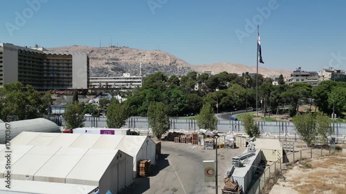 An aerial view captures the new Syrian national flag hoisted on a towering pole in central Damascus, with Mount Qasioun, one of the capital’s most prominent landmarks rising in the background.