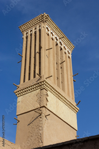 Traditional windcatcher tower in Yazd, Iran, ancient Persian architecture for natural cooling, historic adobe structure against blue sky.
