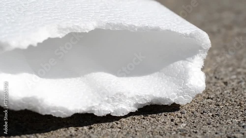 Detailed close-up of white Styrofoam insulation foam with rough broken edges lying on a textured concrete surface highlighting its distinctive cellular material