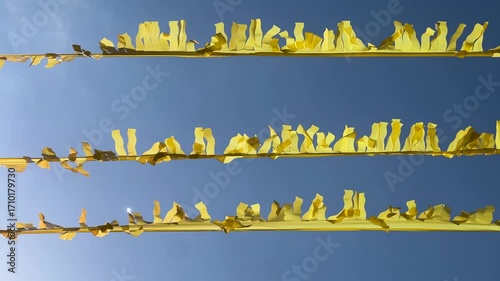 Bright yellow paper streamers fluttering in the wind against a clear blue sky background. Festive decorations for parties or celebrations