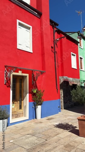 Colorful architecture in Burano island, Venice, Italy. Blue and red painted house against the blue sky. Famous travel destination. Vertical video
