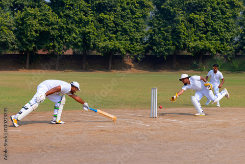 A wicketkeeper dives to catch the ball as a batsman attempts to make his ground on a cricket field