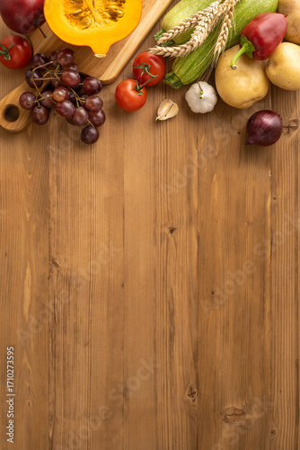 Vertical view of a Thanksgiving harvest featuring fresh fruits, vegetables, and wheat on a wooden surface